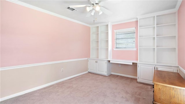 carpeted spare room featuring ceiling fan, built in desk, and crown molding