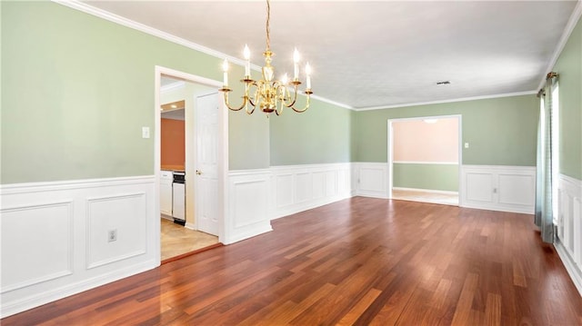 unfurnished dining area featuring wainscoting, wood finished floors, a notable chandelier, and ornamental molding