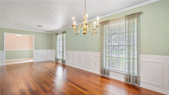 empty room featuring a wainscoted wall, visible vents, an inviting chandelier, wood finished floors, and crown molding