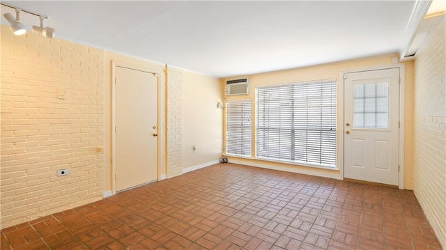 spare room featuring a wall mounted AC, brick wall, and brick patterned floor