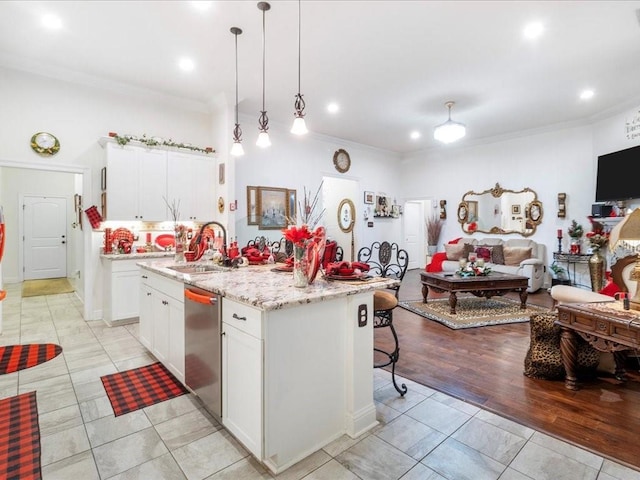 kitchen featuring white cabinetry, light hardwood / wood-style flooring, stainless steel dishwasher, decorative light fixtures, and a kitchen island with sink