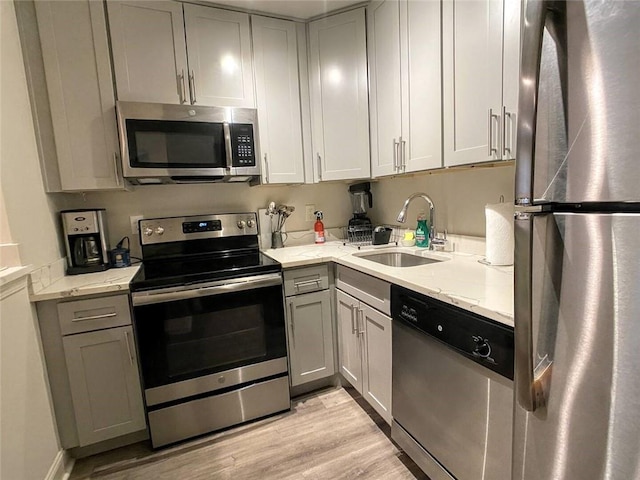 kitchen with light stone counters, light hardwood / wood-style floors, stainless steel appliances, sink, and gray cabinets