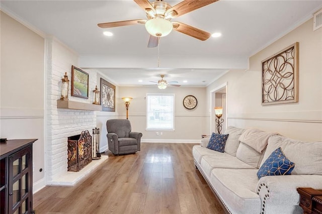 living room with ceiling fan, crown molding, wood-type flooring, and a fireplace