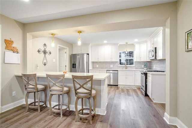 kitchen with a kitchen breakfast bar, light hardwood / wood-style floors, pendant lighting, white cabinets, and appliances with stainless steel finishes