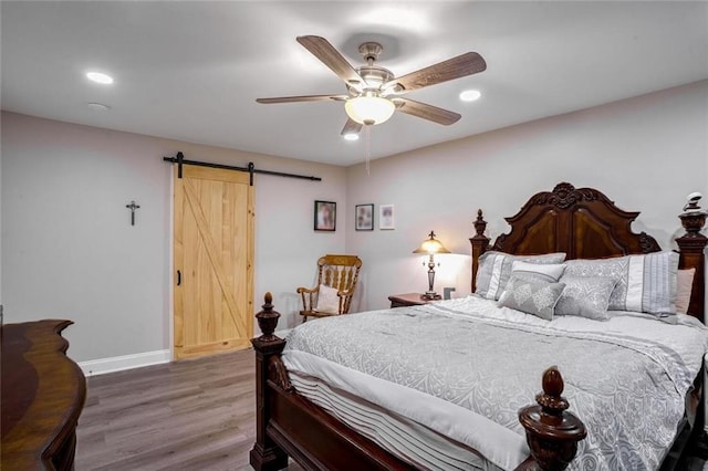 bedroom with hardwood / wood-style floors, a barn door, and ceiling fan