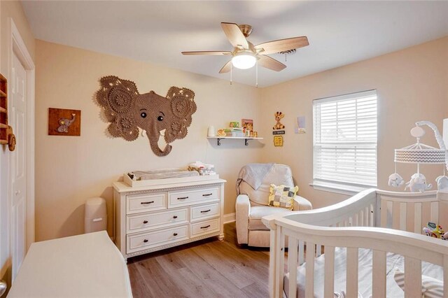 bedroom featuring a crib, light hardwood / wood-style floors, and ceiling fan