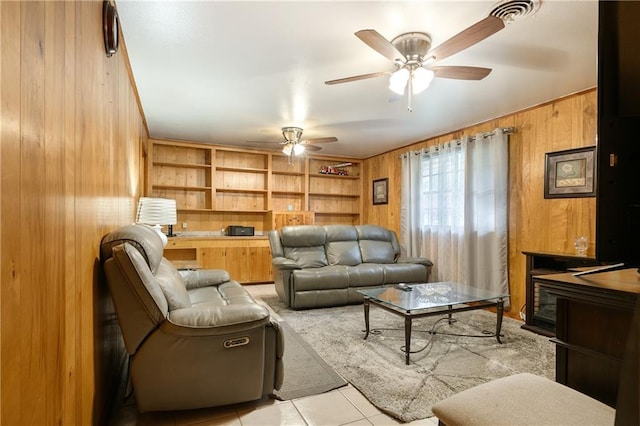 living room featuring ceiling fan, wood walls, light tile patterned flooring, and built in features