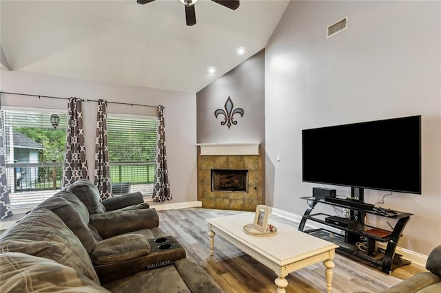 living room featuring ceiling fan, light hardwood / wood-style floors, high vaulted ceiling, and a tiled fireplace