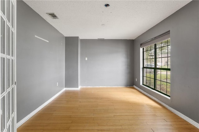 empty room with light wood-type flooring and a textured ceiling