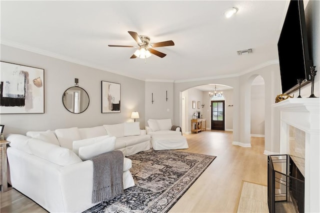 living room with a premium fireplace, ceiling fan with notable chandelier, crown molding, and light hardwood / wood-style floors