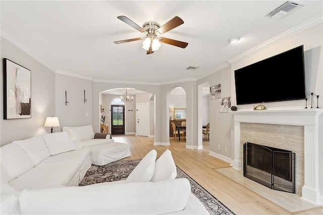 living room with ornamental molding, light wood-type flooring, ceiling fan, and a premium fireplace