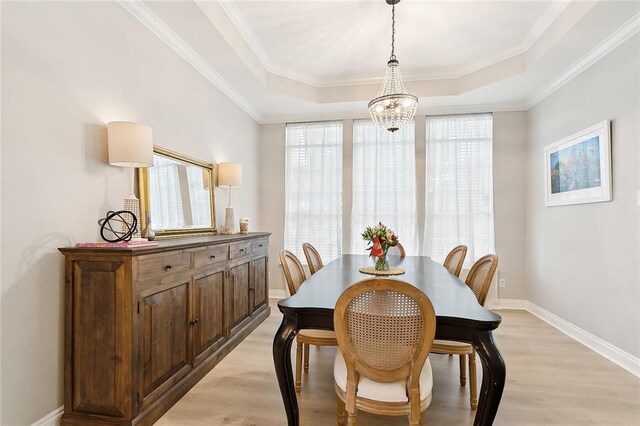 dining space with light wood-type flooring, a raised ceiling, an inviting chandelier, and crown molding