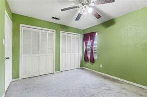 unfurnished bedroom with ceiling fan, light colored carpet, and two closets