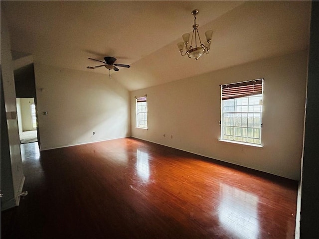 empty room with ceiling fan with notable chandelier, hardwood / wood-style flooring, and vaulted ceiling