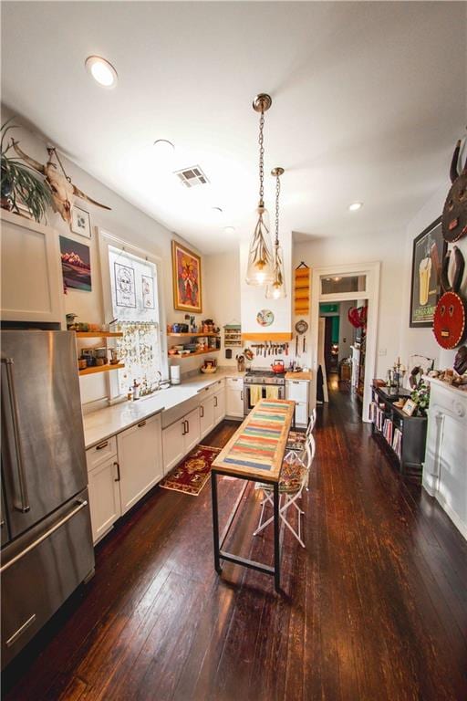 kitchen with dark wood-type flooring, sink, hanging light fixtures, stainless steel fridge, and kitchen peninsula