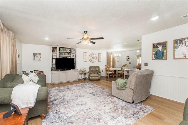 living room with ceiling fan, a textured ceiling, and light wood-type flooring