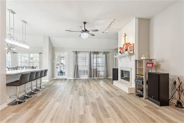 living room with light hardwood / wood-style floors, a textured ceiling, vaulted ceiling, a fireplace, and ceiling fan with notable chandelier