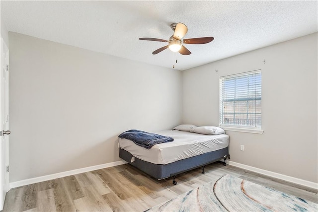 bedroom featuring ceiling fan, light hardwood / wood-style floors, and a textured ceiling