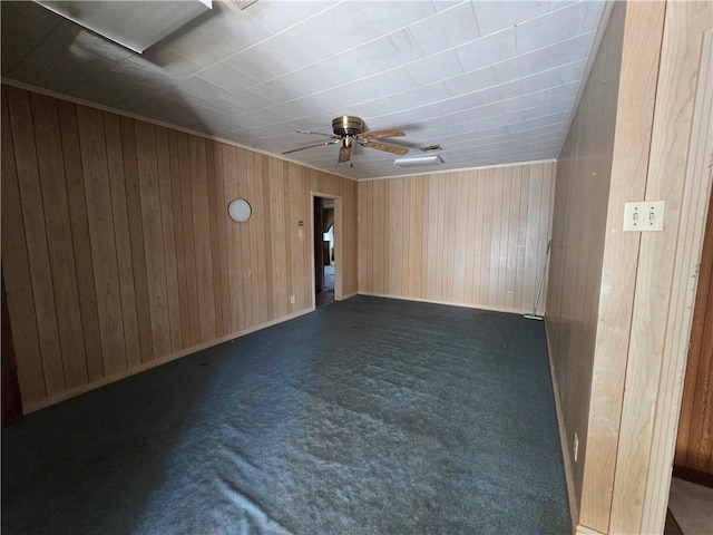 unfurnished room with dark colored carpet, ceiling fan, and wood walls