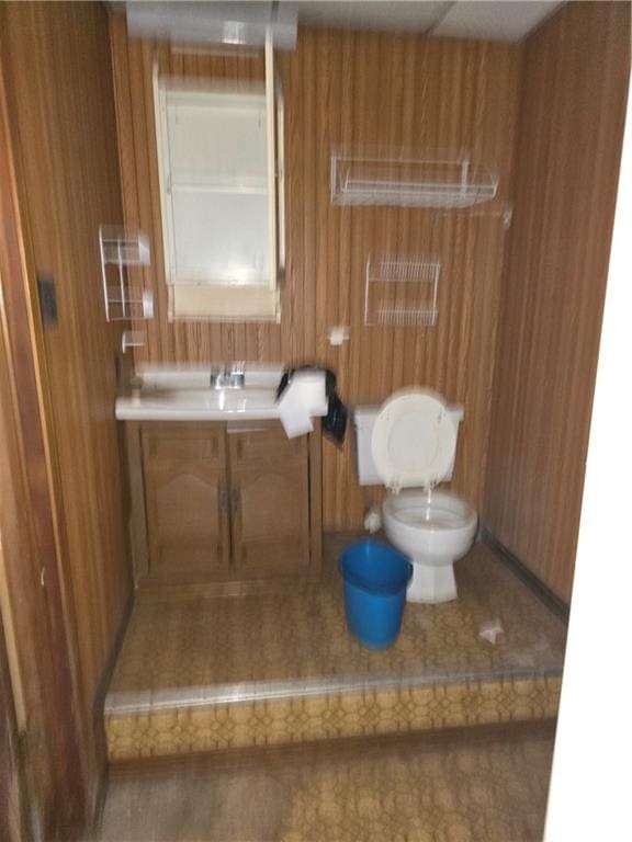 bathroom featuring wooden walls, vanity, and toilet