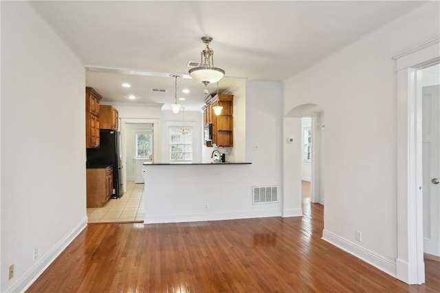 kitchen with kitchen peninsula, black fridge, decorative light fixtures, and light hardwood / wood-style flooring