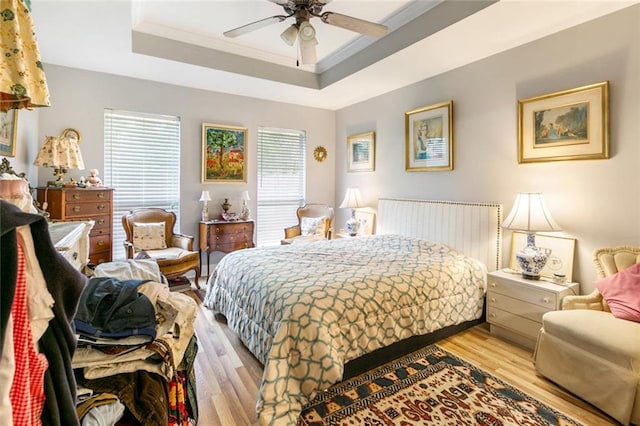 bedroom featuring ceiling fan, light hardwood / wood-style floors, crown molding, and a tray ceiling