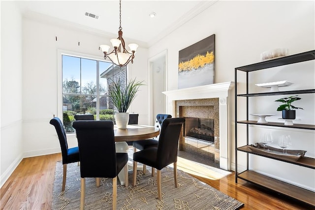 dining area with an inviting chandelier, hardwood / wood-style floors, crown molding, and a premium fireplace