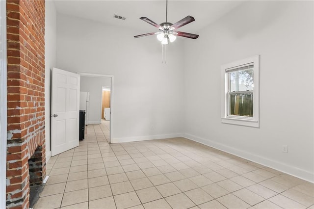 empty room with ceiling fan, high vaulted ceiling, light tile patterned flooring, and a brick fireplace