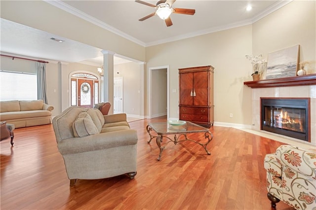 living room featuring decorative columns, a tile fireplace, light hardwood / wood-style flooring, and ornamental molding