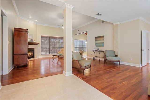 living area featuring ceiling fan, ornate columns, crown molding, and light hardwood / wood-style flooring