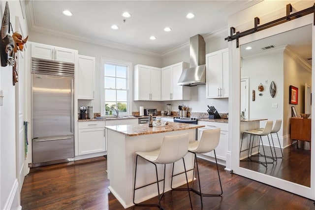 kitchen with wall chimney range hood, a breakfast bar, a center island, and stainless steel built in refrigerator