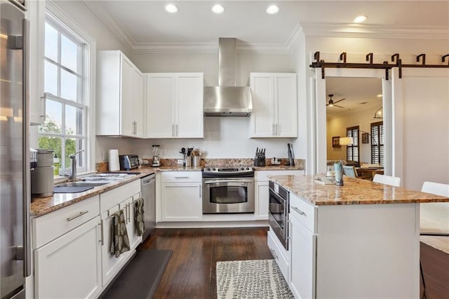 kitchen featuring wall chimney exhaust hood, stainless steel appliances, a barn door, white cabinets, and dark hardwood / wood-style floors