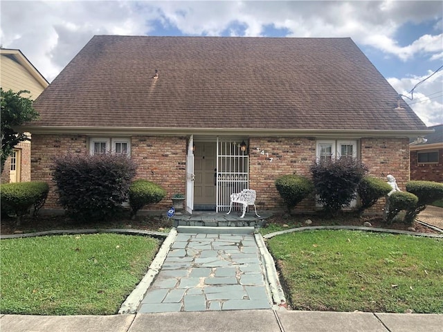 view of front of home with brick siding, roof with shingles, and a front yard