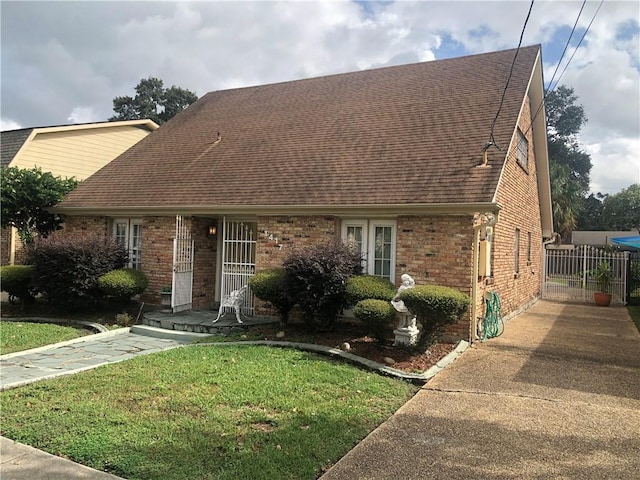 view of front of house featuring a shingled roof, a front yard, brick siding, and fence