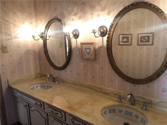 full bath with double vanity, wallpapered walls, and a sink