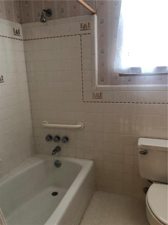 bathroom with toilet, a tub, and tile walls