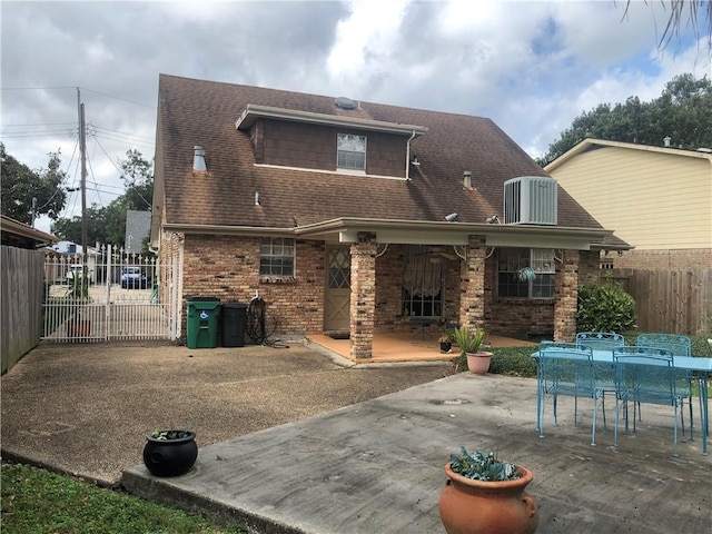 rear view of house with brick siding, roof with shingles, fence, and a patio