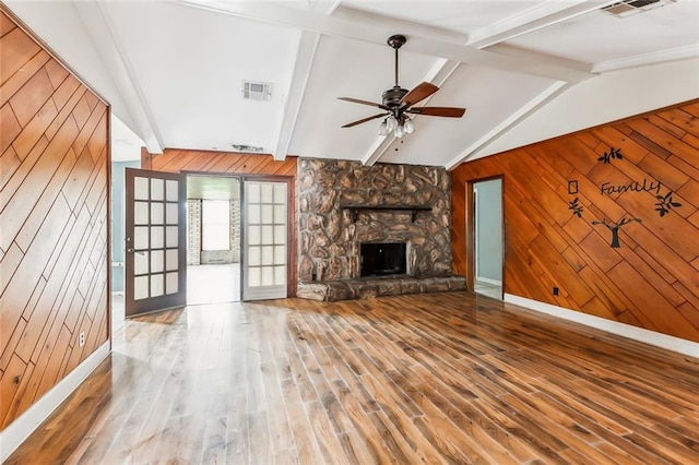 unfurnished living room with hardwood / wood-style floors, lofted ceiling with beams, a stone fireplace, wooden walls, and ceiling fan