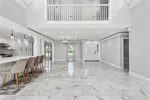 foyer featuring ornamental molding, a towering ceiling, and ornate columns