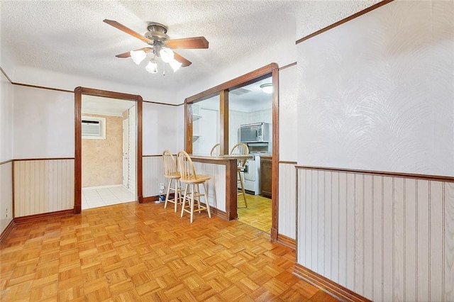 empty room featuring a textured ceiling, light parquet floors, ceiling fan, and an AC wall unit