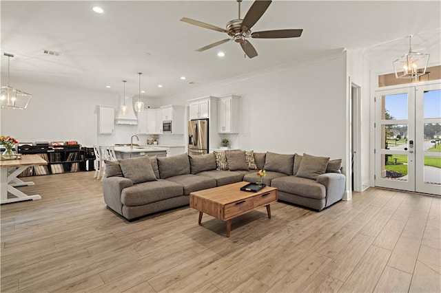 living room featuring sink, french doors, light hardwood / wood-style floors, ceiling fan with notable chandelier, and ornamental molding