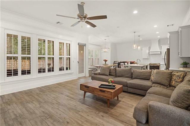 living room featuring ceiling fan with notable chandelier, light wood-type flooring, and crown molding