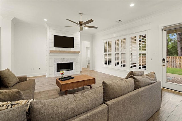 living room featuring ceiling fan, a large fireplace, crown molding, and light wood-type flooring