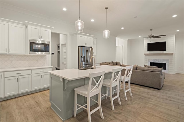 kitchen featuring white cabinets, an island with sink, decorative light fixtures, light hardwood / wood-style floors, and stainless steel appliances