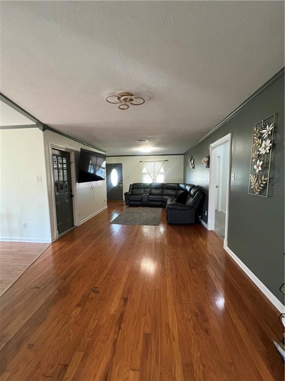 unfurnished living room featuring wood-type flooring, a textured ceiling, and ornamental molding