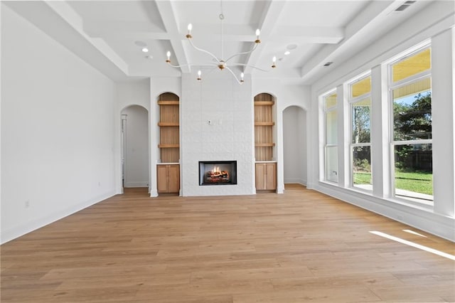 unfurnished living room featuring a large fireplace, light hardwood / wood-style flooring, beam ceiling, and an inviting chandelier