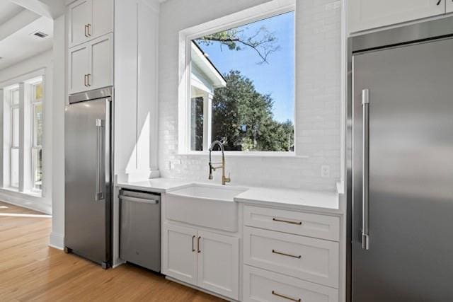 kitchen with sink, decorative backsplash, light wood-type flooring, appliances with stainless steel finishes, and white cabinetry