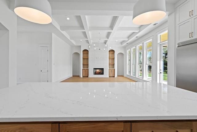 kitchen with light stone counters, coffered ceiling, stainless steel built in refrigerator, a large fireplace, and beamed ceiling