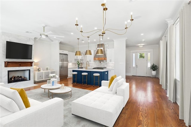 living room with hardwood / wood-style floors, ceiling fan with notable chandelier, crown molding, and sink