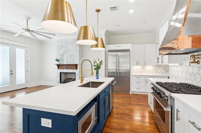 kitchen featuring custom exhaust hood, blue cabinets, sink, built in appliances, and white cabinets